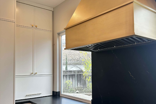 Minimal brass range hood above a black marble backsplash in a modern kitchen.