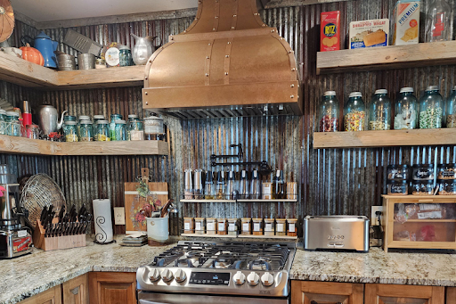 Rustic kitchen with a copper range hood, corrugated metal backsplash, and open wood shelves.