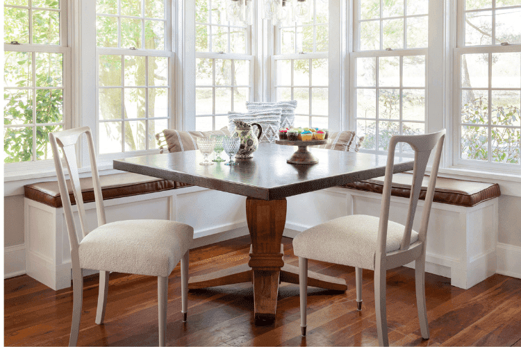 Bright breakfast nook with wooden table, chairs, and large windows.