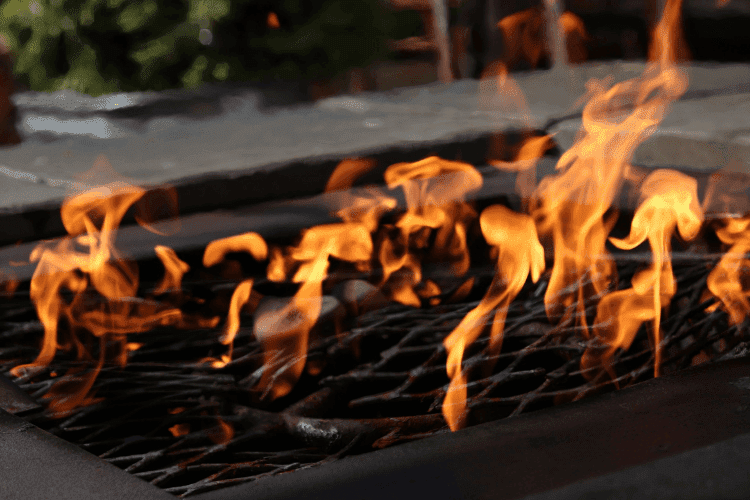 Bright orange flames flickering through a metal grate inside a stone fire pit.