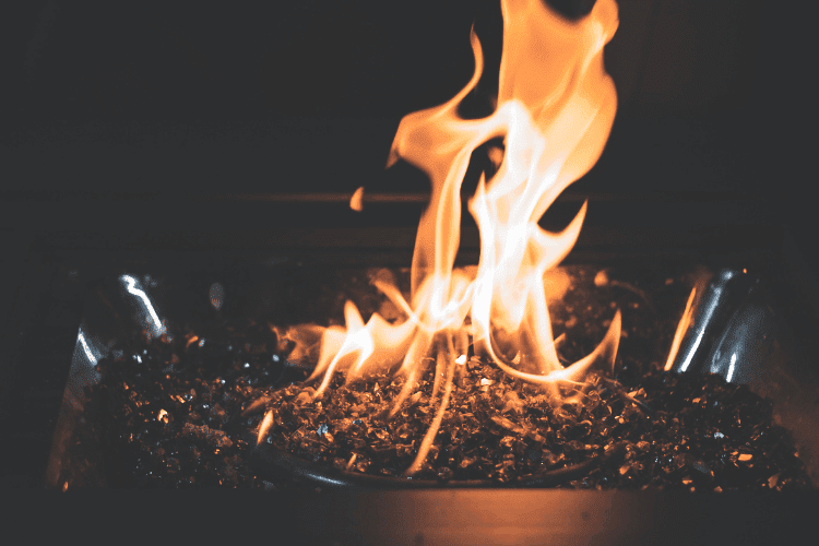 Close-up of orange flames rising from black fire glass in a modern fire pit.