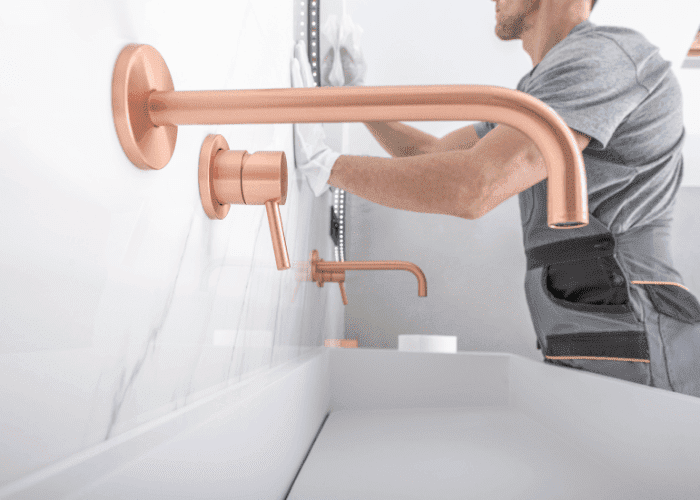 Plumber installing a copper wall-mounted faucet above a modern bathtub.