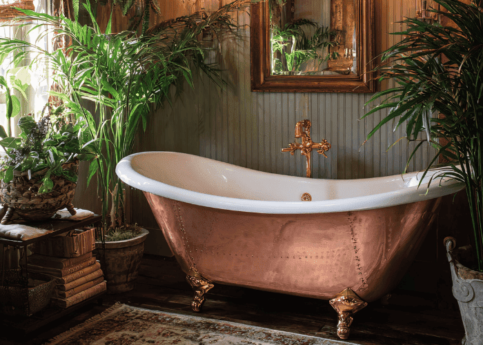 Luxury bathroom featuring a copper clawfoot bathtub surrounded by lush plants.