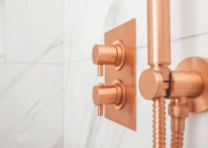 Modern brushed copper shower controls mounted on a marble bathroom wall.