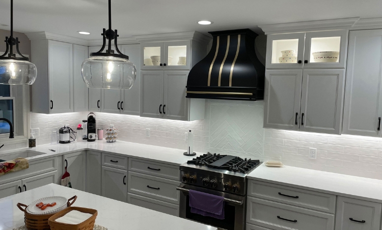 Modern kitchen with black and gold range hood, white cabinets, and pendant lighting.