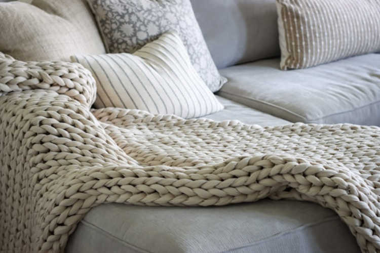Cozy living room sofa with a chunky knit throw blanket and neutral pillows.