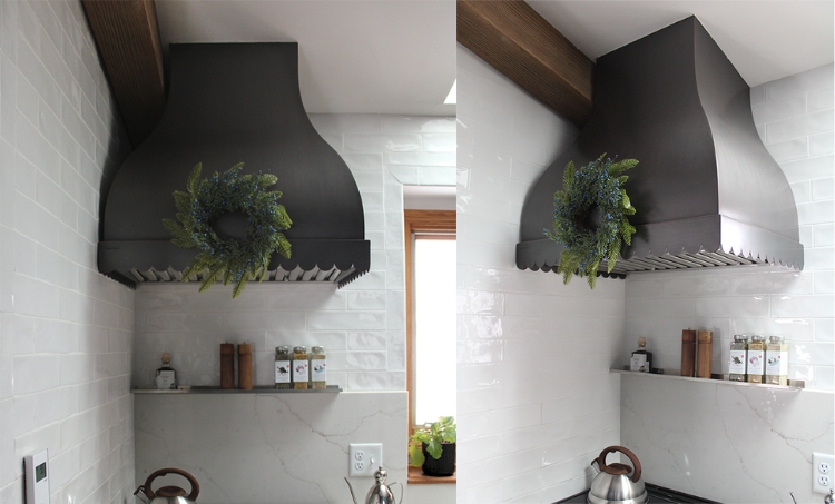 Matte black stainless steel range hood with a green wreath above a stove, set against white tile walls and a small spice shelf.