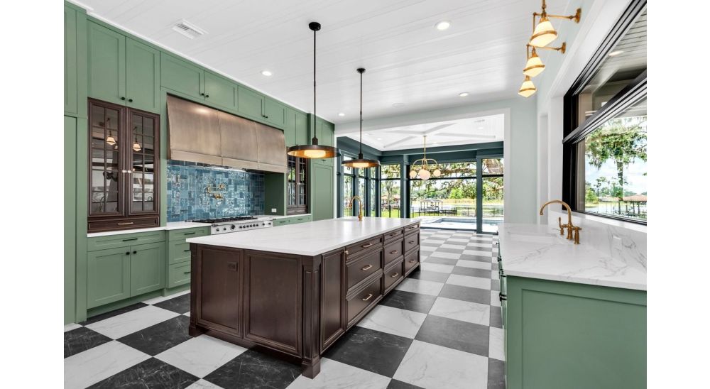 Luxury kitchen with avocado green cabinets, a dark wood island, custom metal range hood, brass fixtures, and black and white checkered flooring.