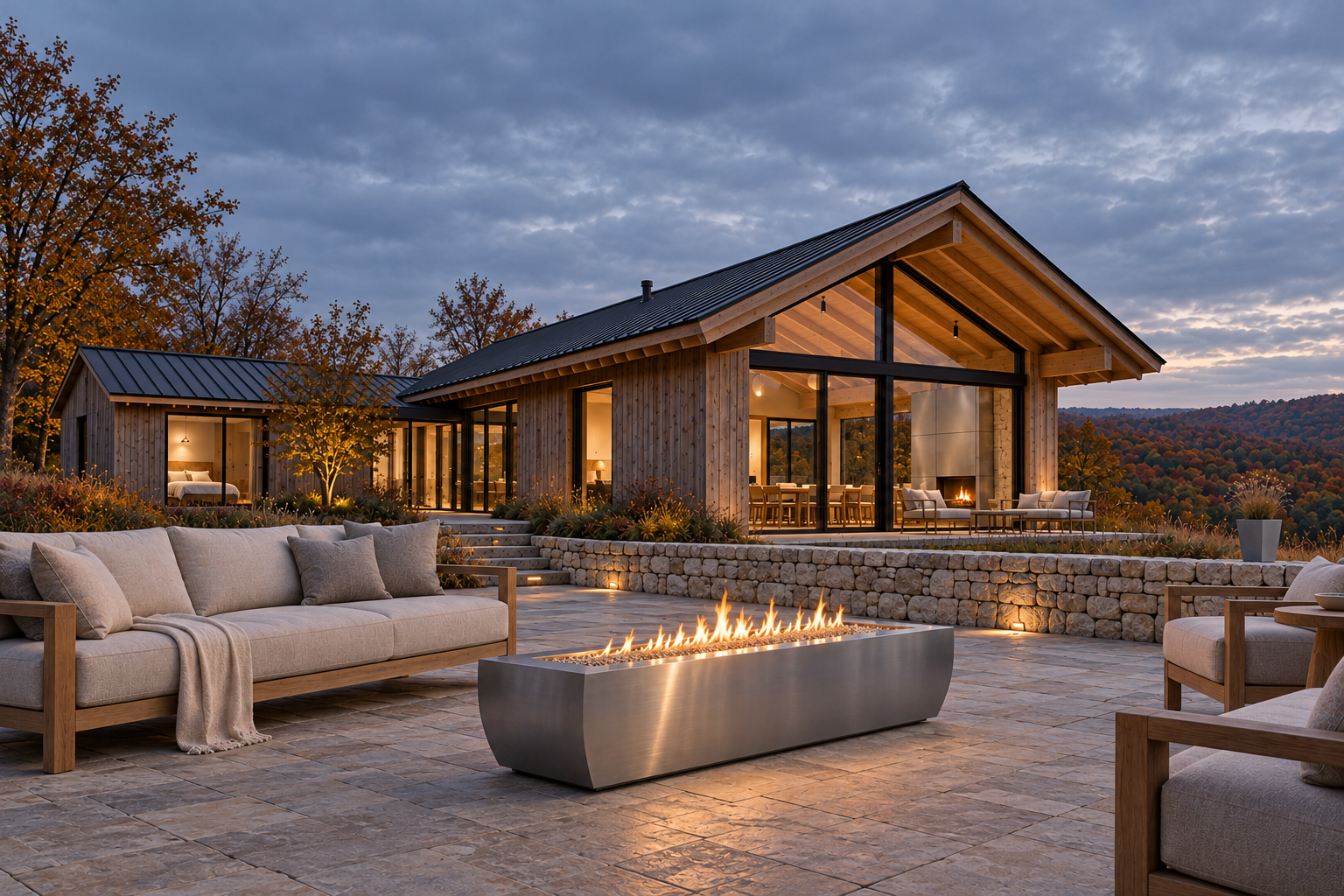 Rectangular stainless fire pit on a stone terrace outside a glazed timber home at dusk.