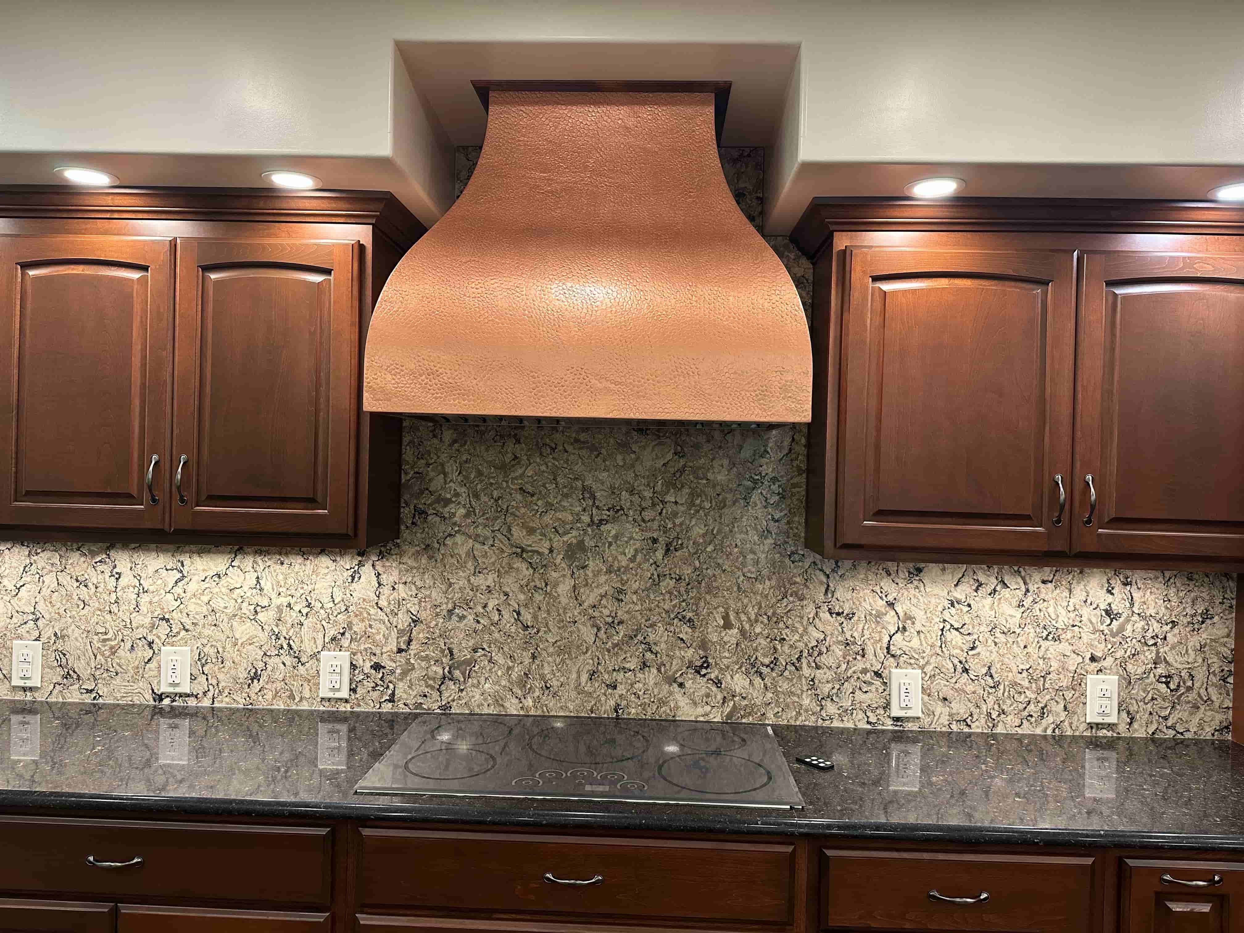 CopperSmith Artisan AT1 Old Coin Copper Kitchen Range Hood in a craftsman style features wood cabinets black countertops marble backsplash