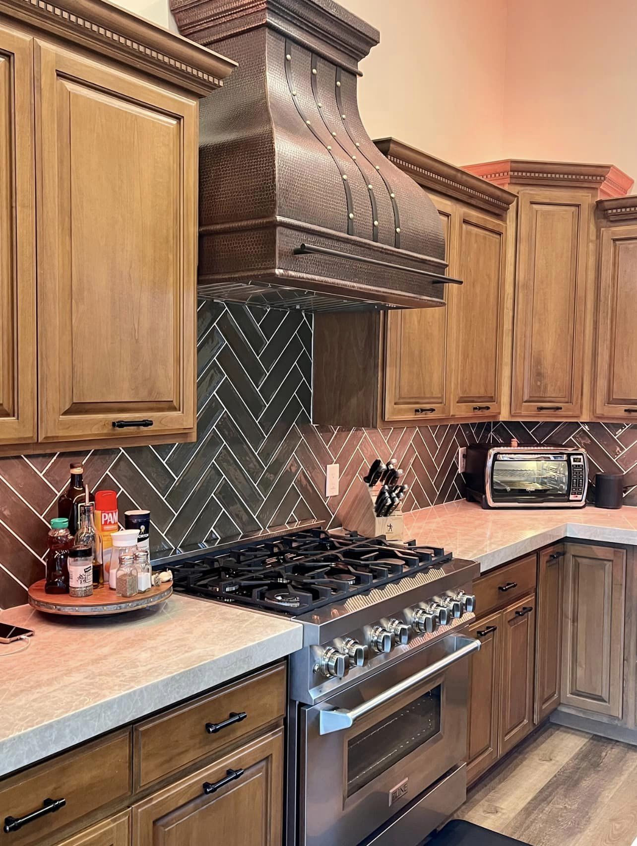 A french kitchen design with brown kitchen cabinets features a range hood, complemented, marble kitchen countertops beautiful marble backsplash