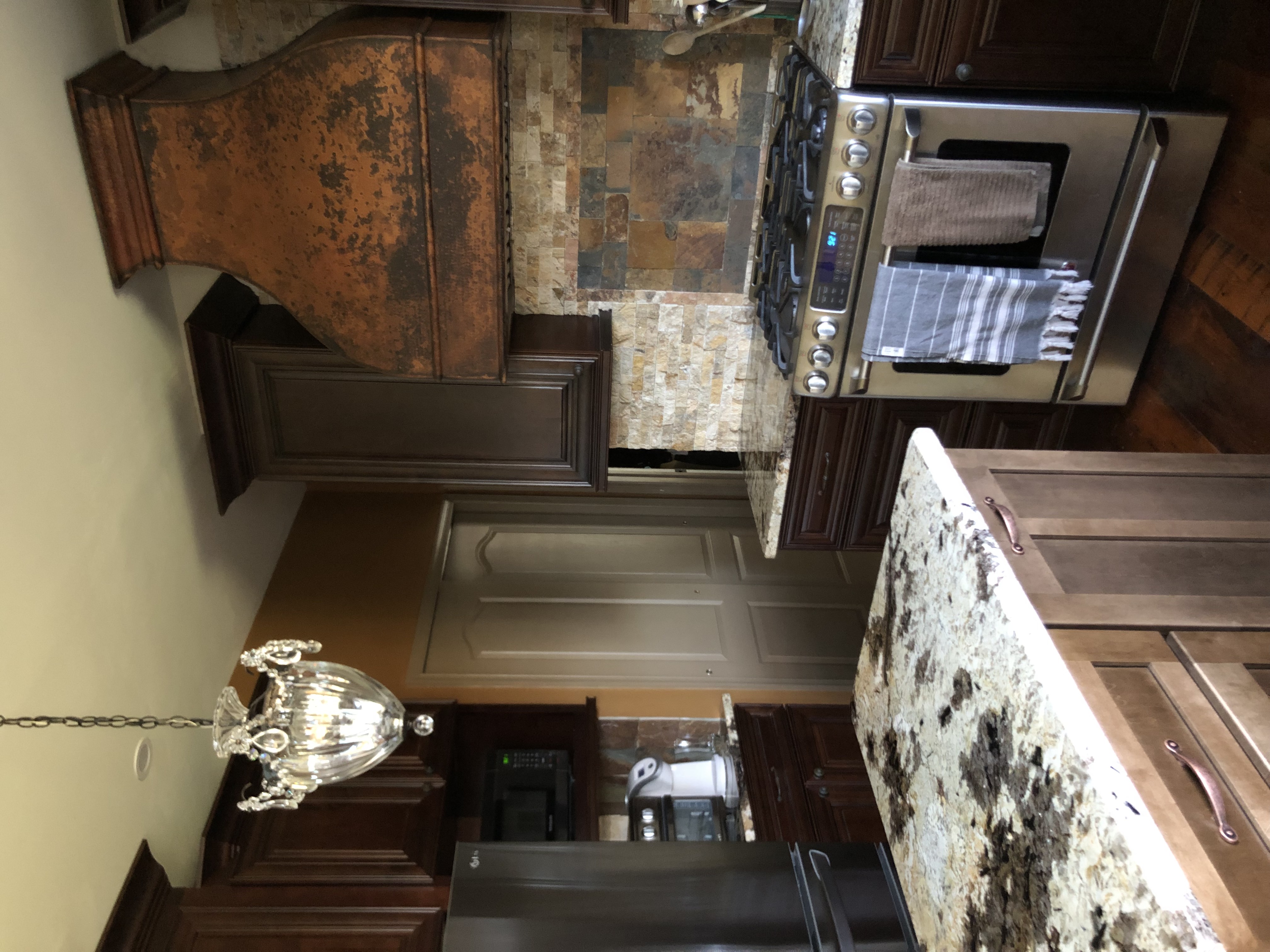 Rustic kitchen with brown cabinets, marble countertops, brick backsplash, complemented by a sleek range hood design