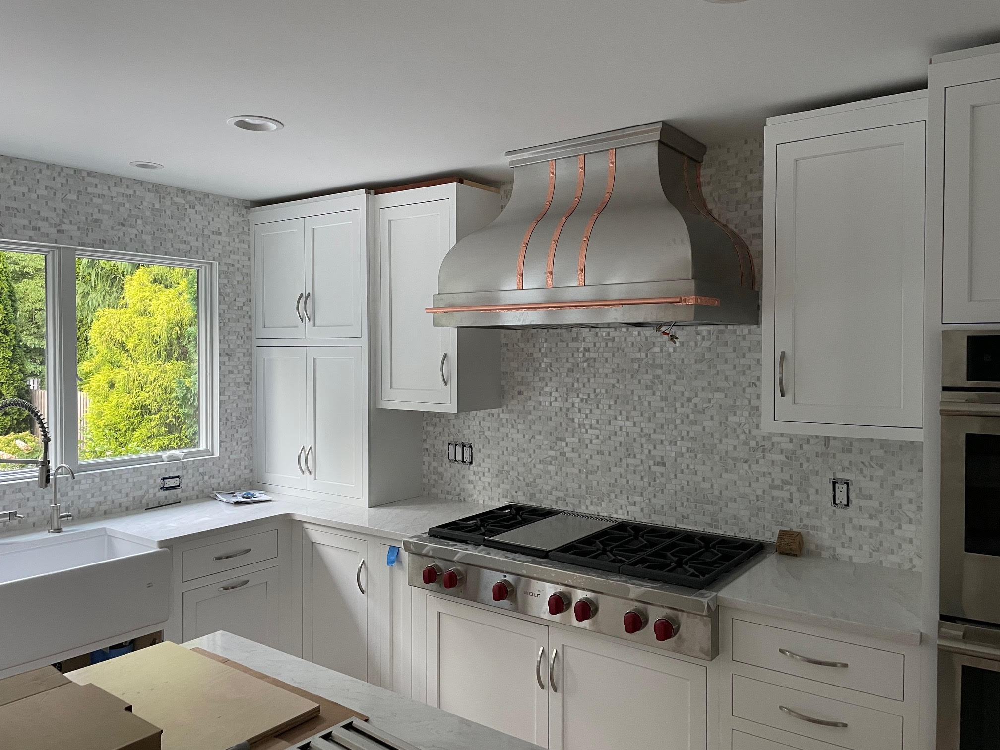 Charming kitchen design with range hood, white cabinets, marble countertops and brick backsplash