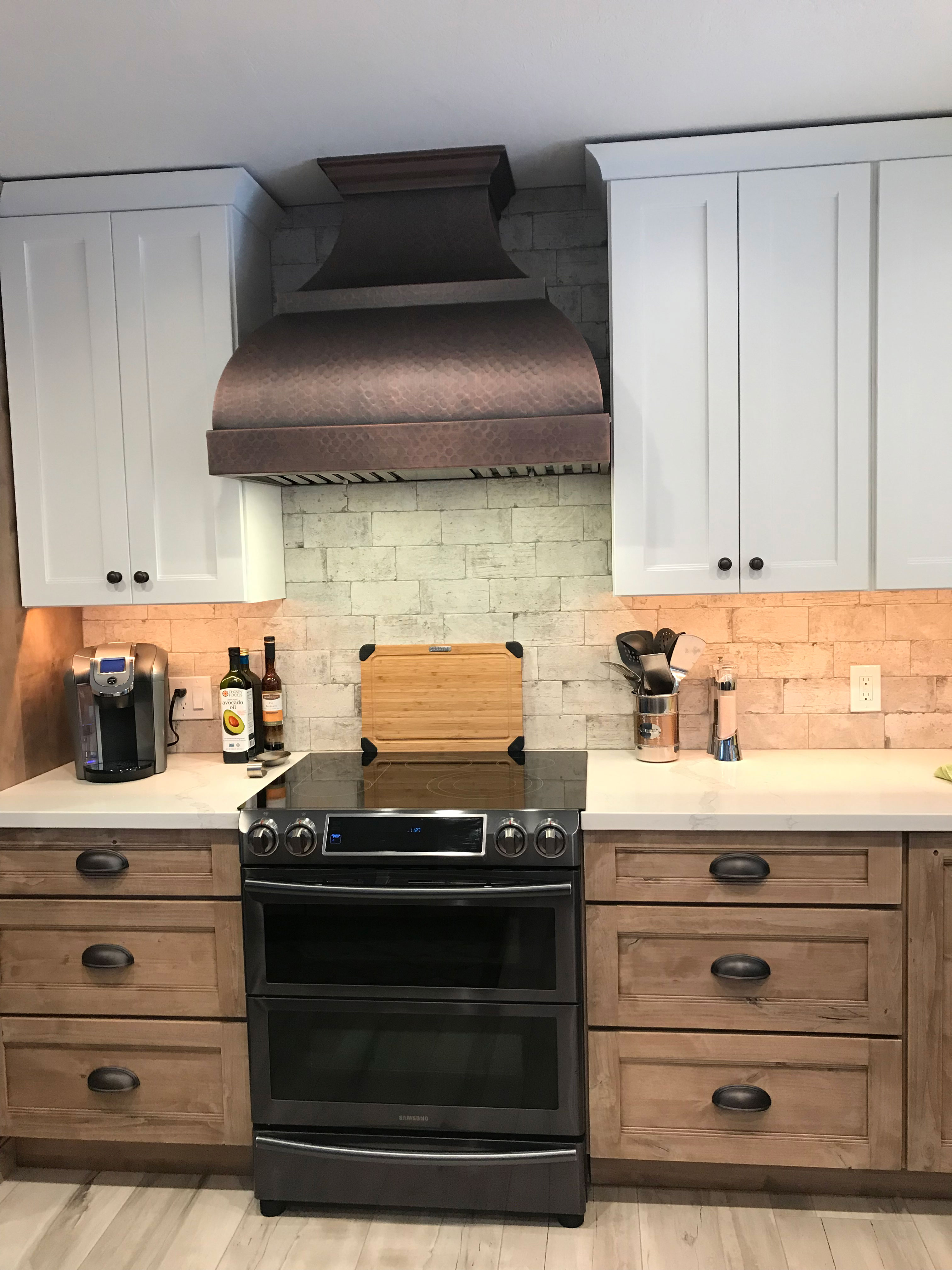 Copper range hood with industrial kitchen renovations,incorporating wood kitchen cabinets with marble kitchen countertops brick backsplash