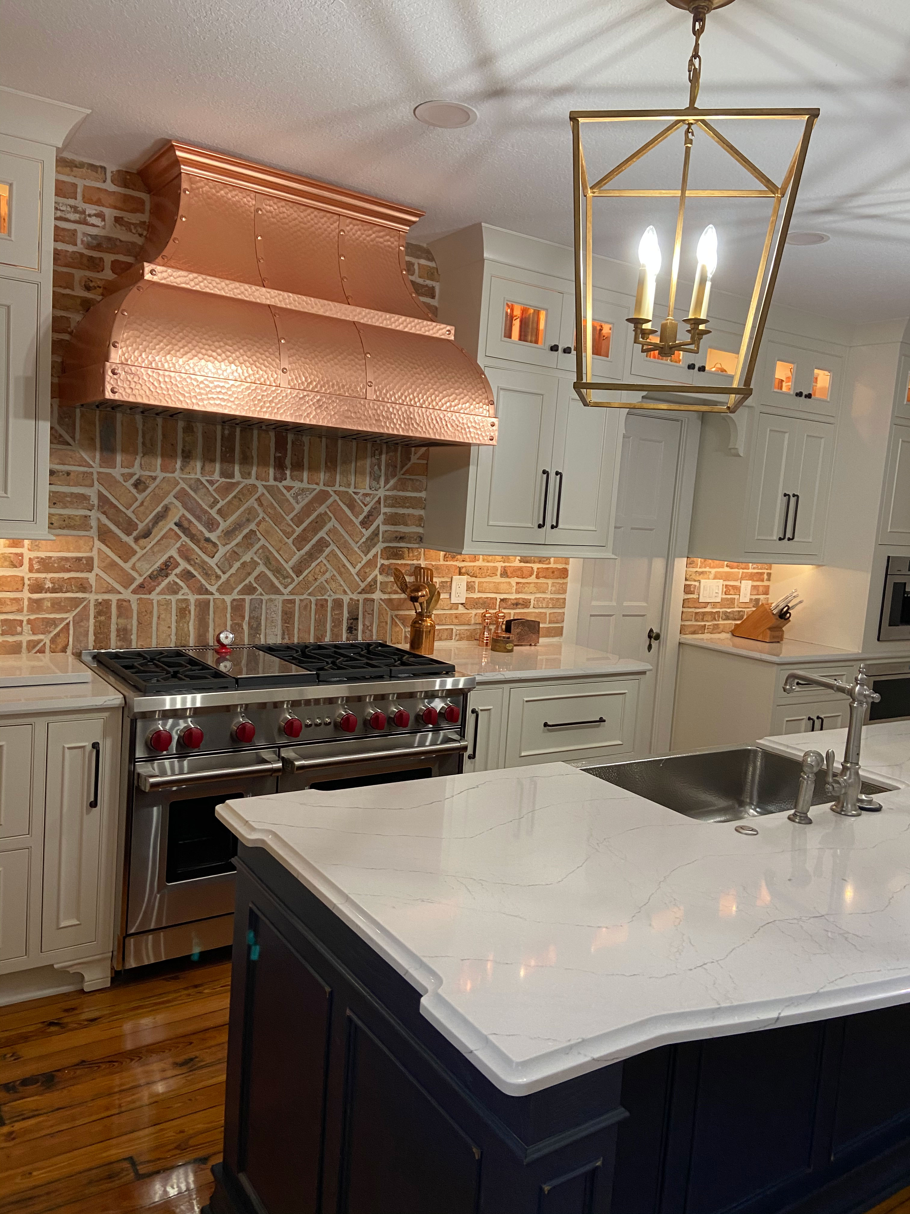 Incorporating white kitchen cabinets with copper range hood, marble kitchen countertops brick backsplash