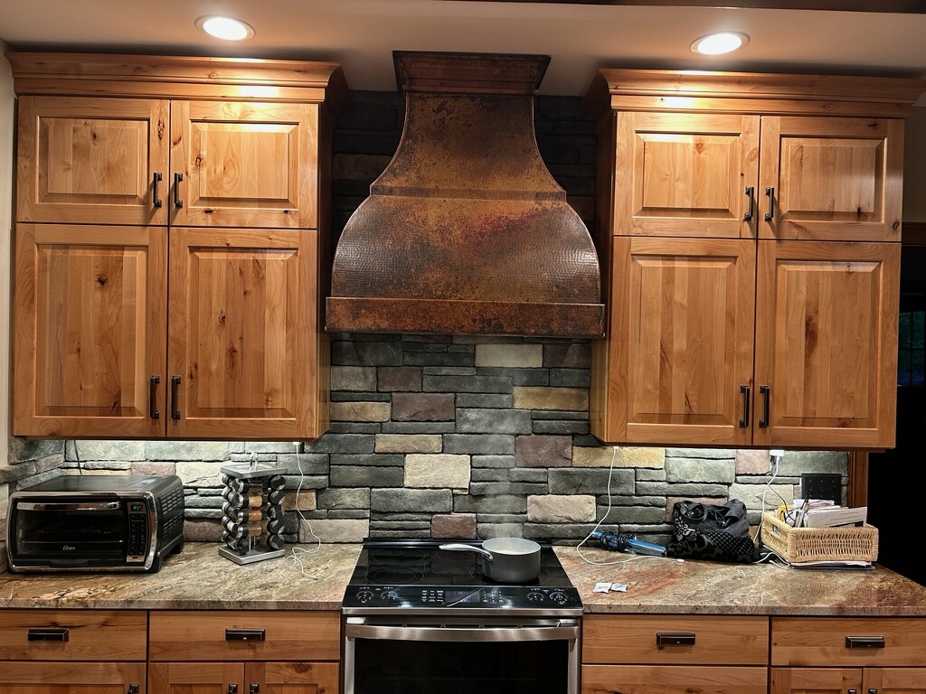 French-inspired kitchen design featuring sleek brown cabinets, marble countertops, brick backsplash, crowned by a stunning range hood