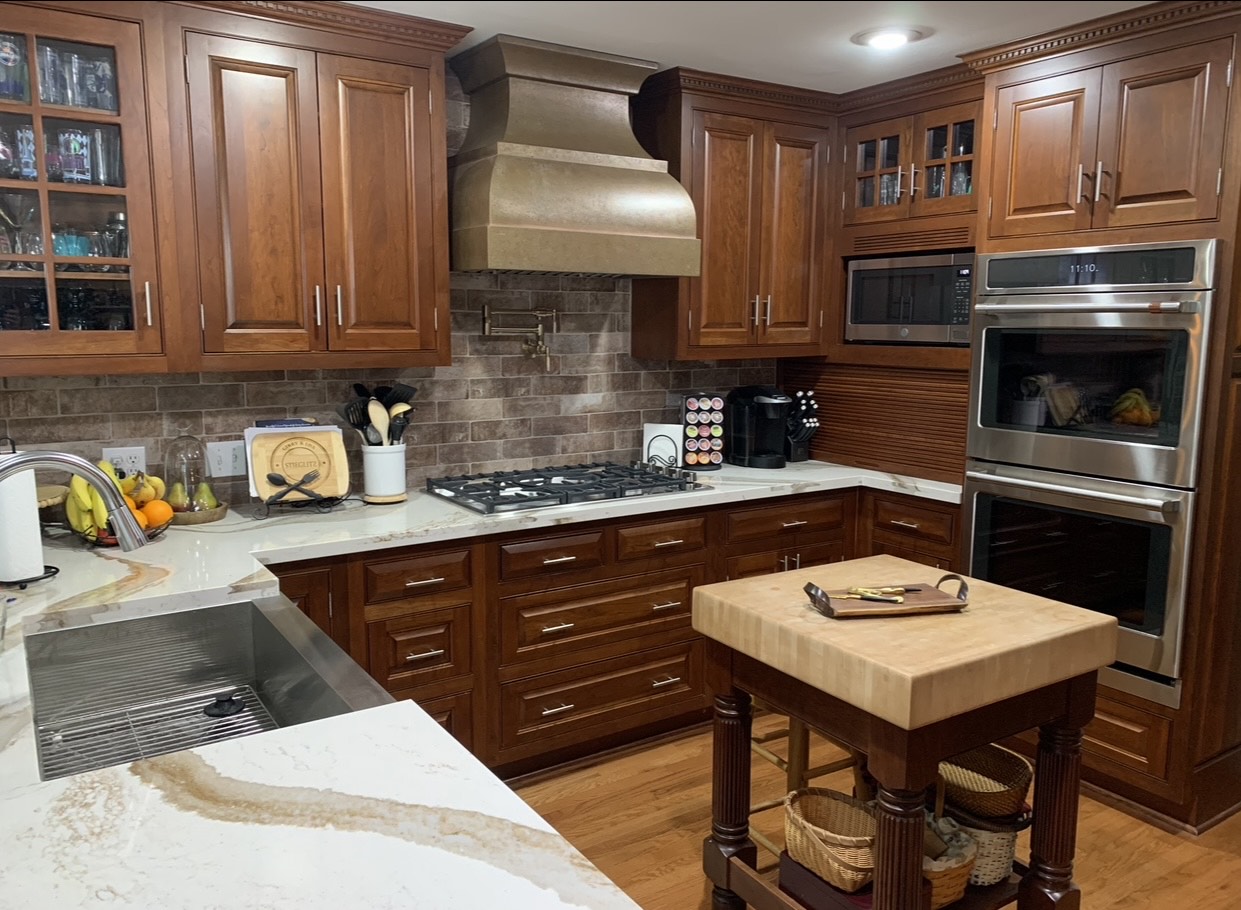 Copper range hood into your cottage kitchen design with wood kitchen cabinets, white kitchen countertops, charming brick backsplash