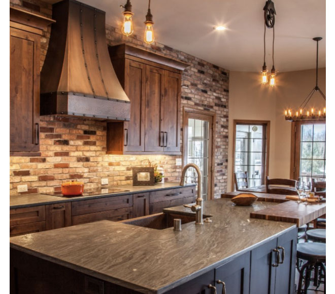 Luxurious kitchen design idea featuring elegant range hood with beautiful brown kitchen cabinets, and luxurious marble kitchen and brick backsplash