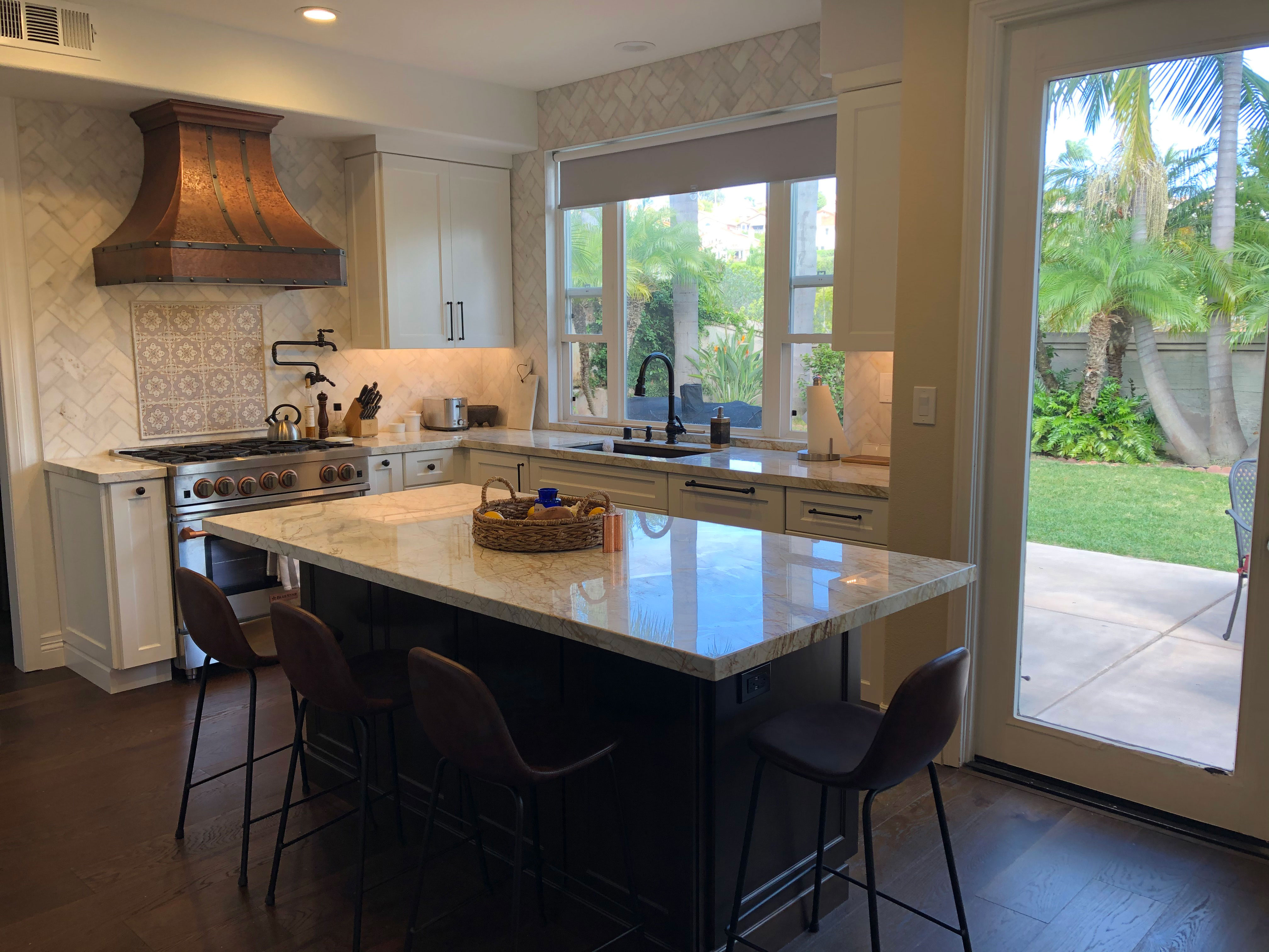 With brown kitchen cabinets brick backsplash, the french kitchen design is enhanced by white kitchen countertops stylish range hood