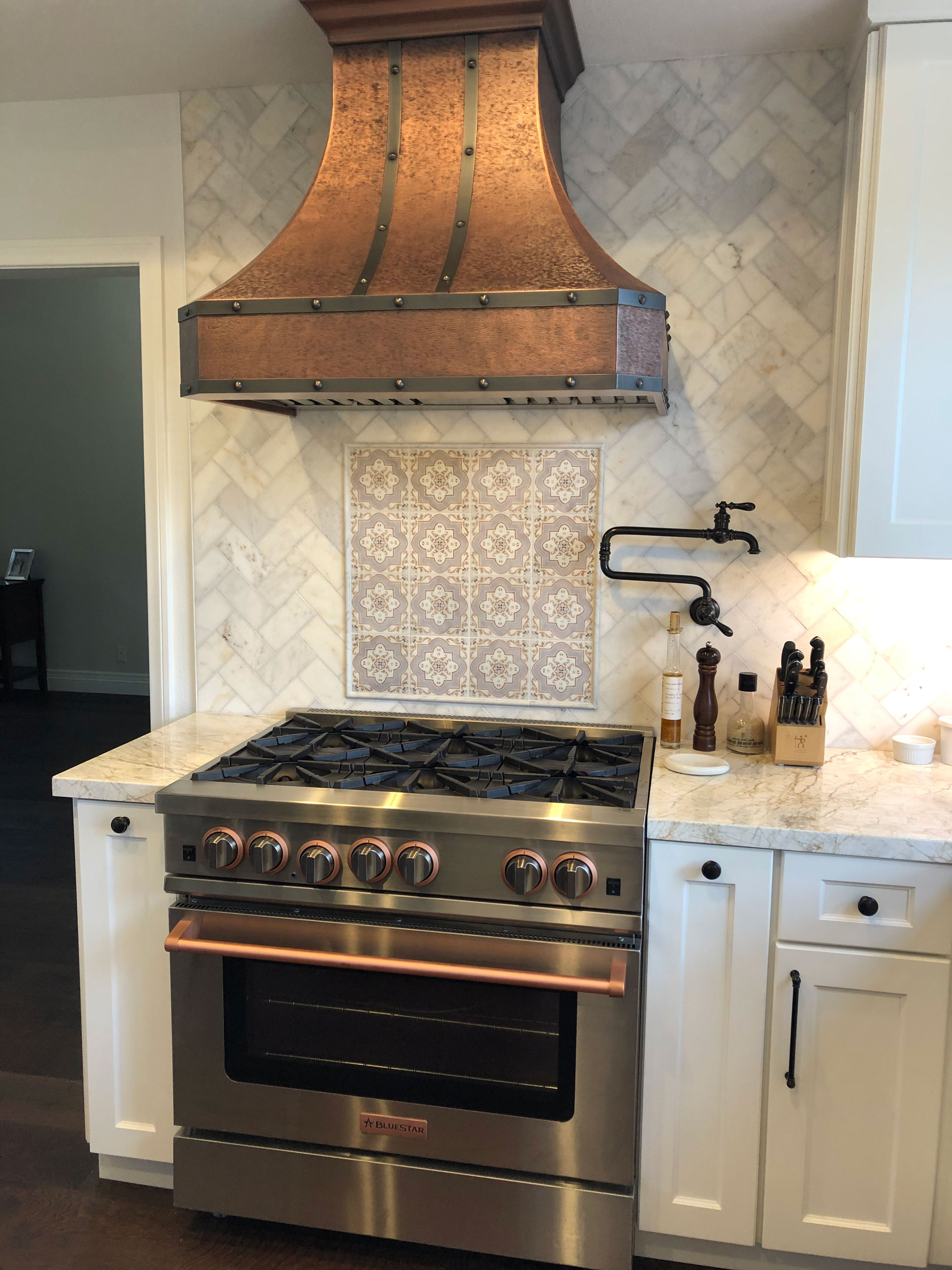 French kitchen design features brown kitchen cabinets with marble kitchen countertops, brick backsplash stylish range hood