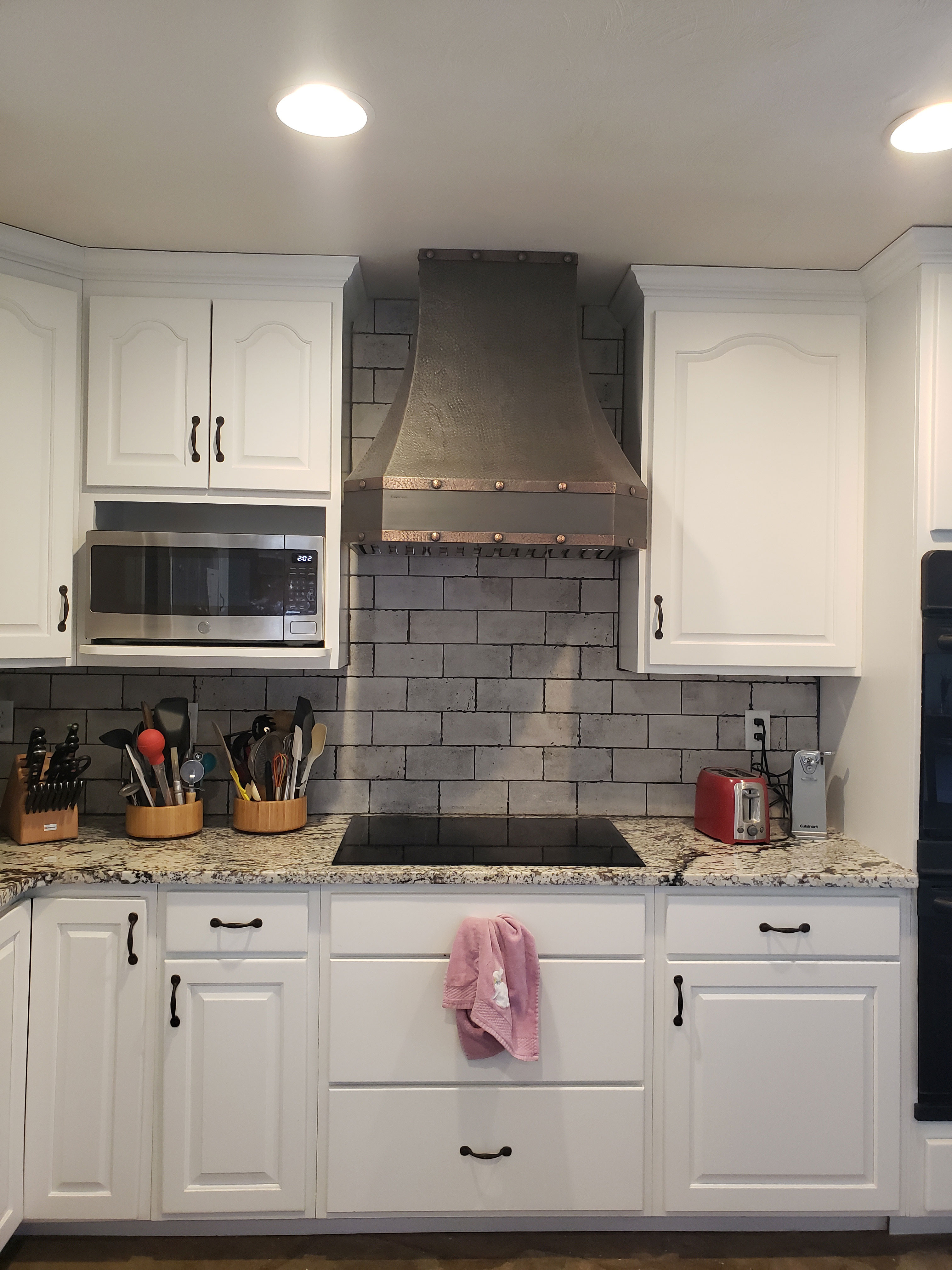 Beautiful french kitchen design with stylish range hood and white kitchen cabinets, marble kitchen countertops and brick backsplash