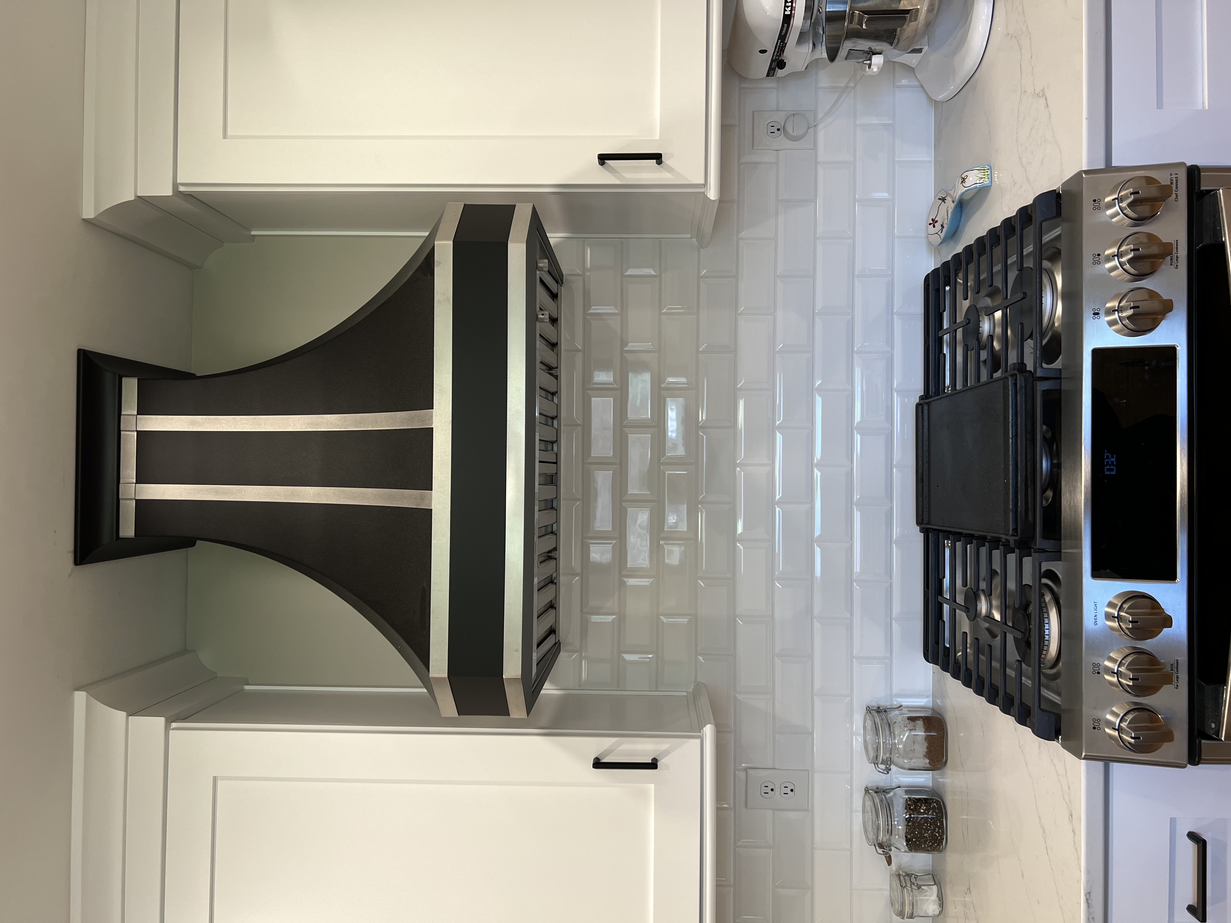 Modern kitchen design idea with unique range hood, sleek white kitchen cabinets, black kitchen countertops, white tile backsplash and with french-inspired elements