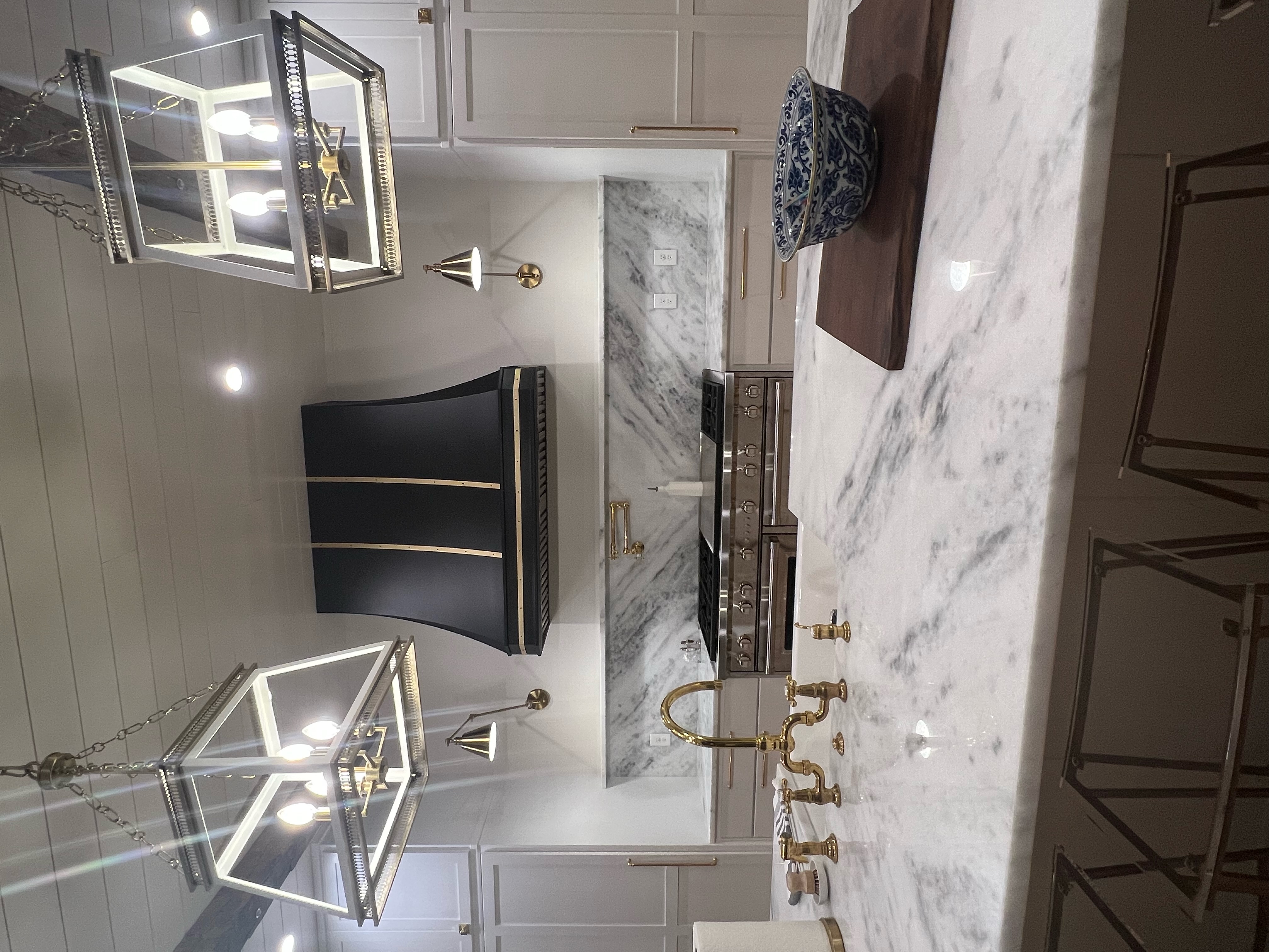 Stunning coastal kitchen with white kitchen cabinets, marble kitchen countertops, beautiful marble backsplash complemented by a stylish range hood