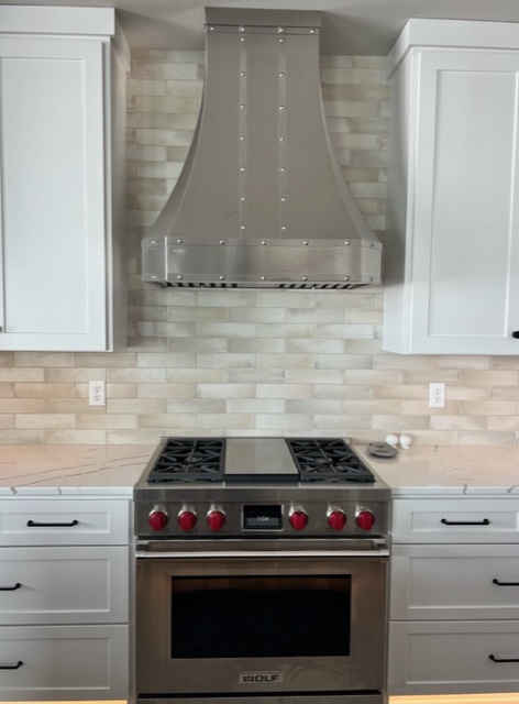 Classic kitchen with white cabinets and countertops features a brick backsplash, complemented by a stylish range hood