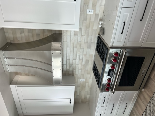 A classic kitchen design idea with white kitchen cabinets and countertops, featuring a stylish range hood charming brick backsplash,