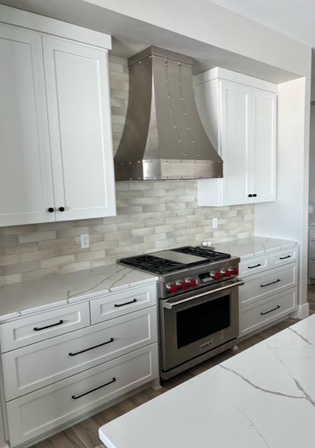 Classic kitchen with white kitchen cabinets and countertops, complemented by a brick backsplash stylish range hood