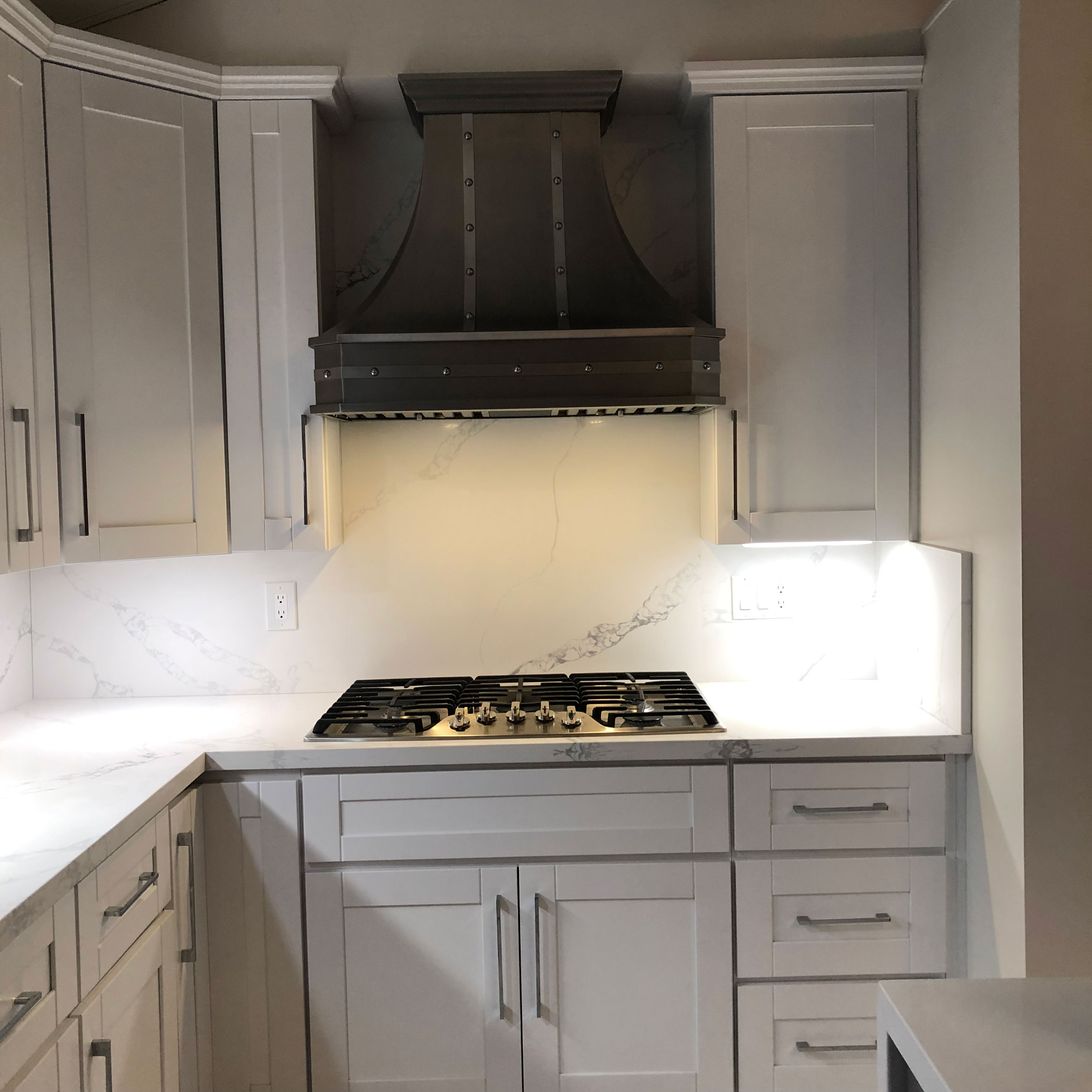 Kitchen design featuring, inspired range hood, white kitchen cabinets, exquisite marble kitchen countertops,marble backsplash
