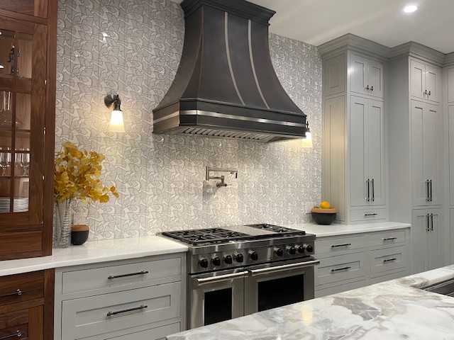 CopperSmith Classic CX4 Wall Mount Antique Brass Range Hood n a classic style kitchen with Marble countertops white cabinets and white tile backsplash