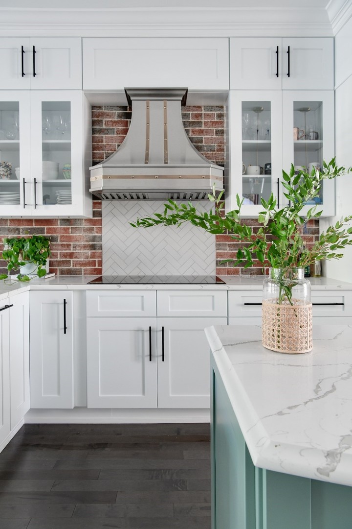 A stunning french kitchen design featuring white kitchen cabinets, marble kitchen countertops, marble backsplash, stylish range hood
