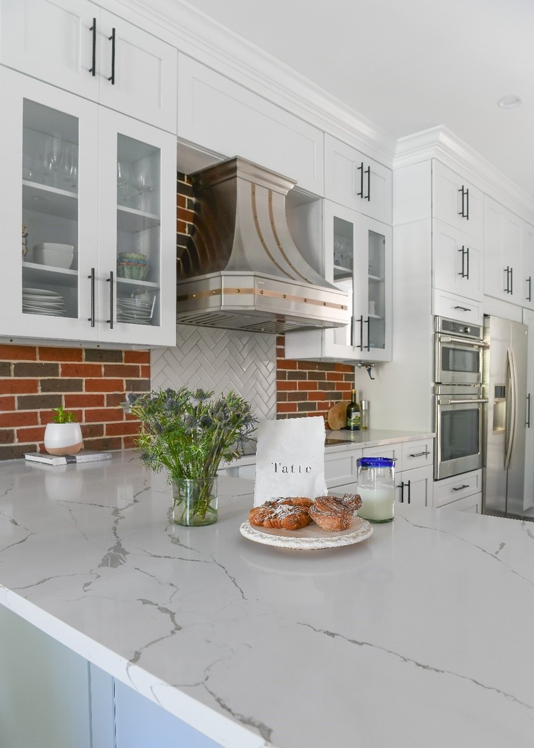 Sleek white kitchen with marble countertops stylish brick backsplash, featuring a modern kitchen table, french kitchen design