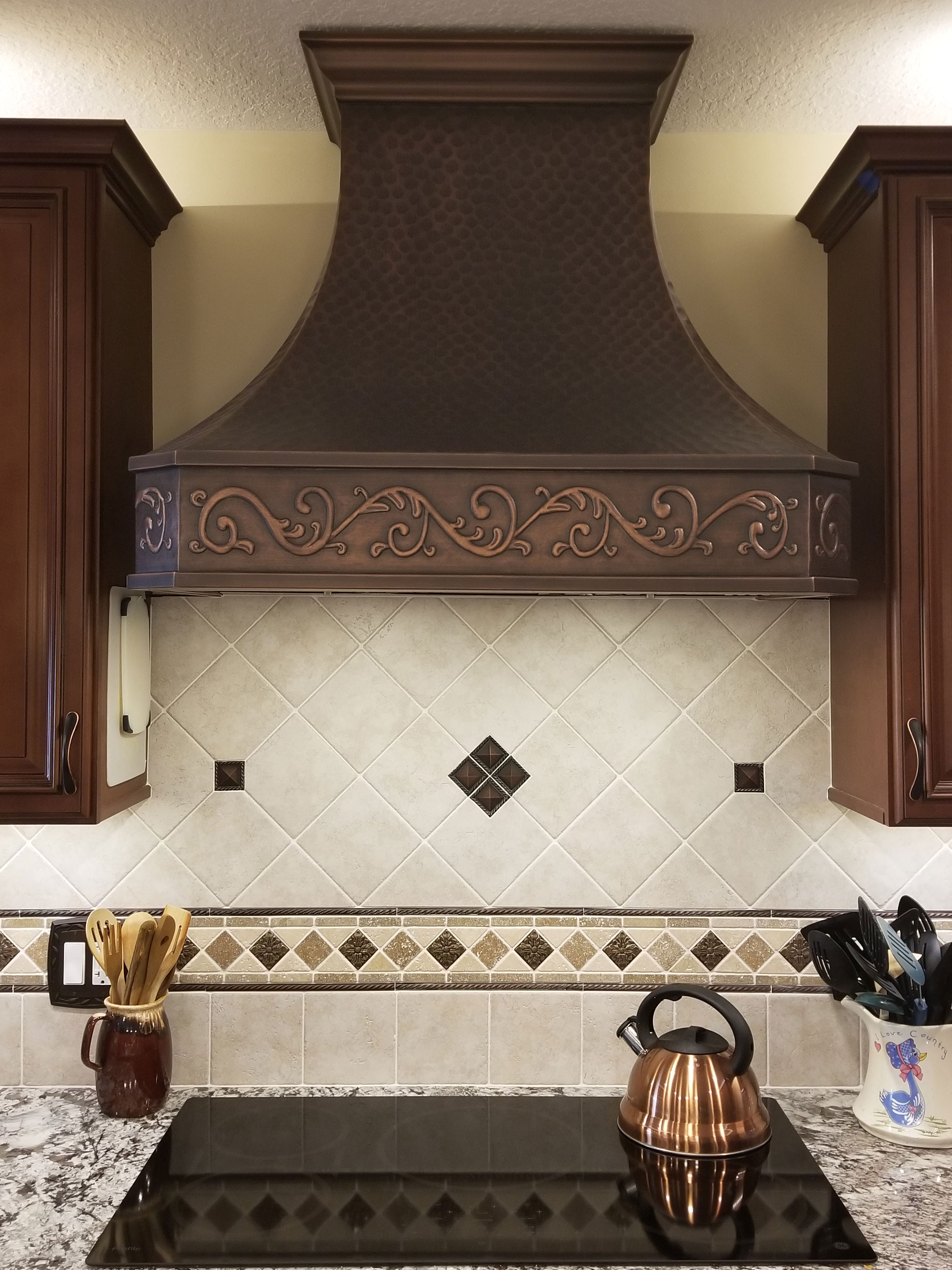 Embellished range hood over an electric stove with tea kettle