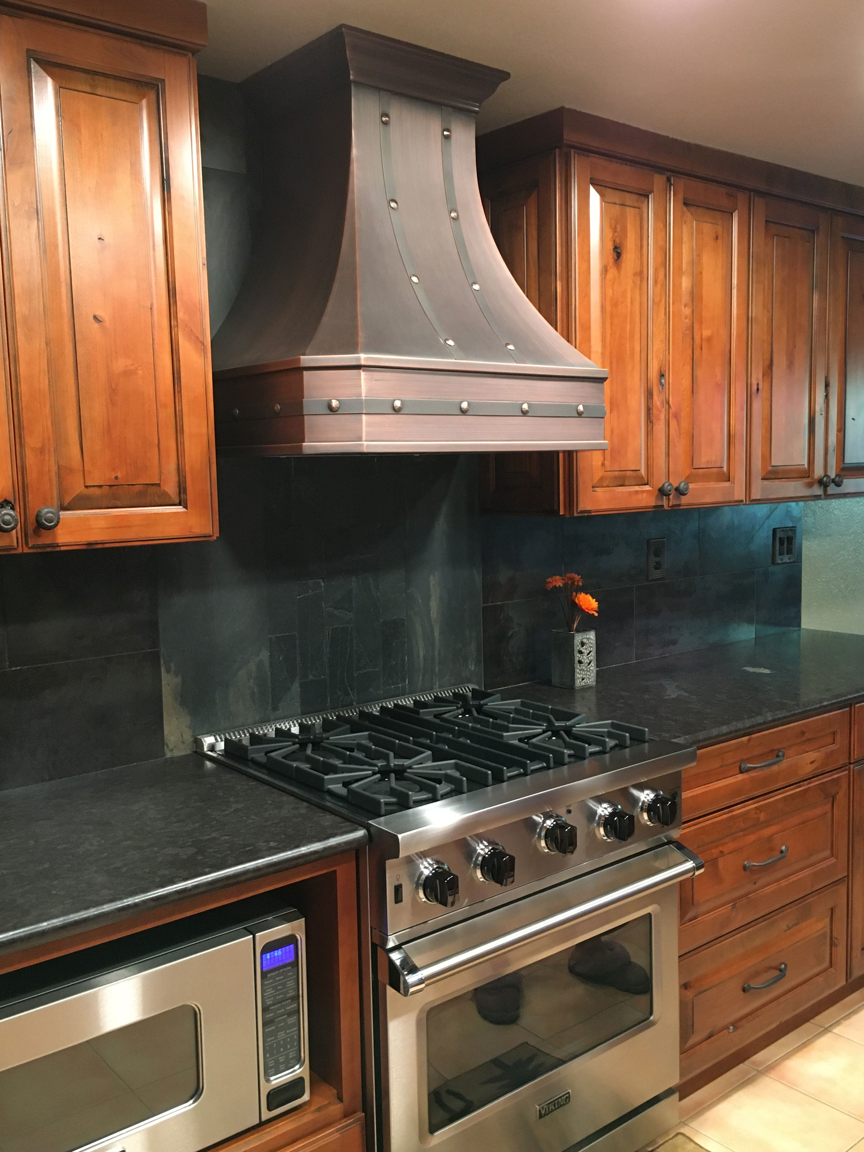 Kitchen design idea incorporating,copper range hood, brown cabinets,sleek black kitchen countertops striking marble backsplash with