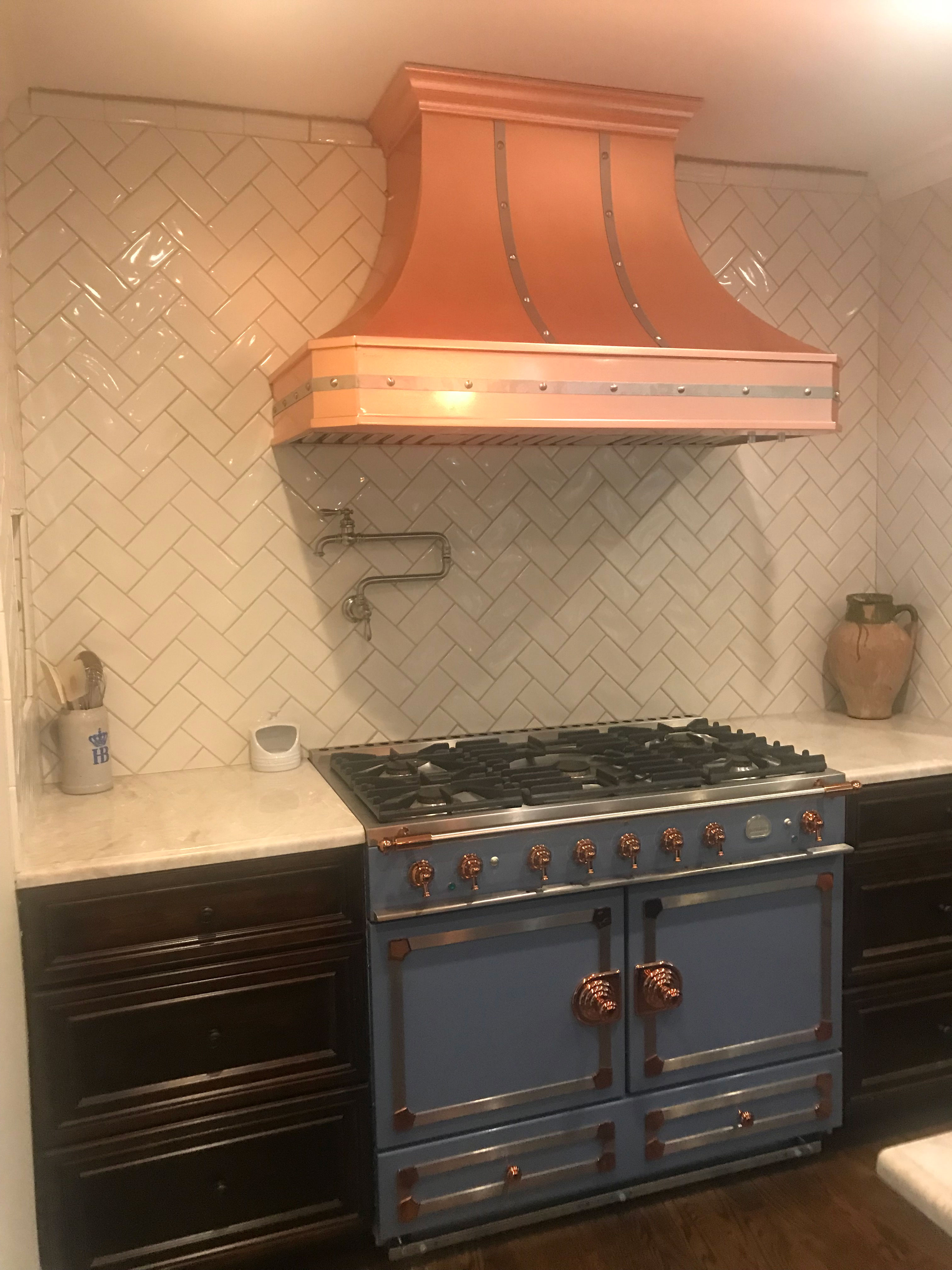 French kitchen design featuring rich brown cabinets, luxurious marble countertops brick backsplash range hood
