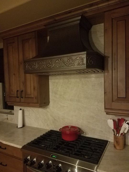 A copper range hood with a dark, aged finish and vine leaf motif World CopperSmith