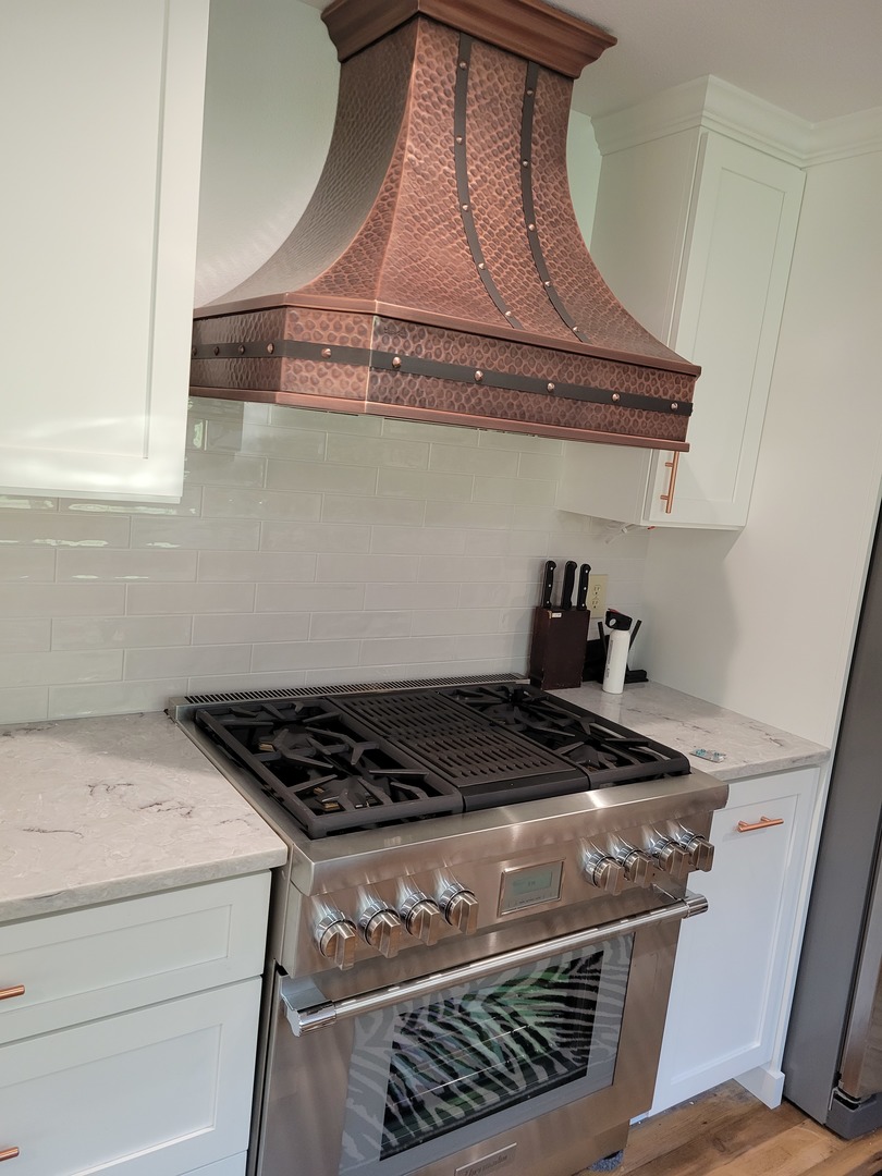 Two-tone copper range hood with white tile backsplash and stove