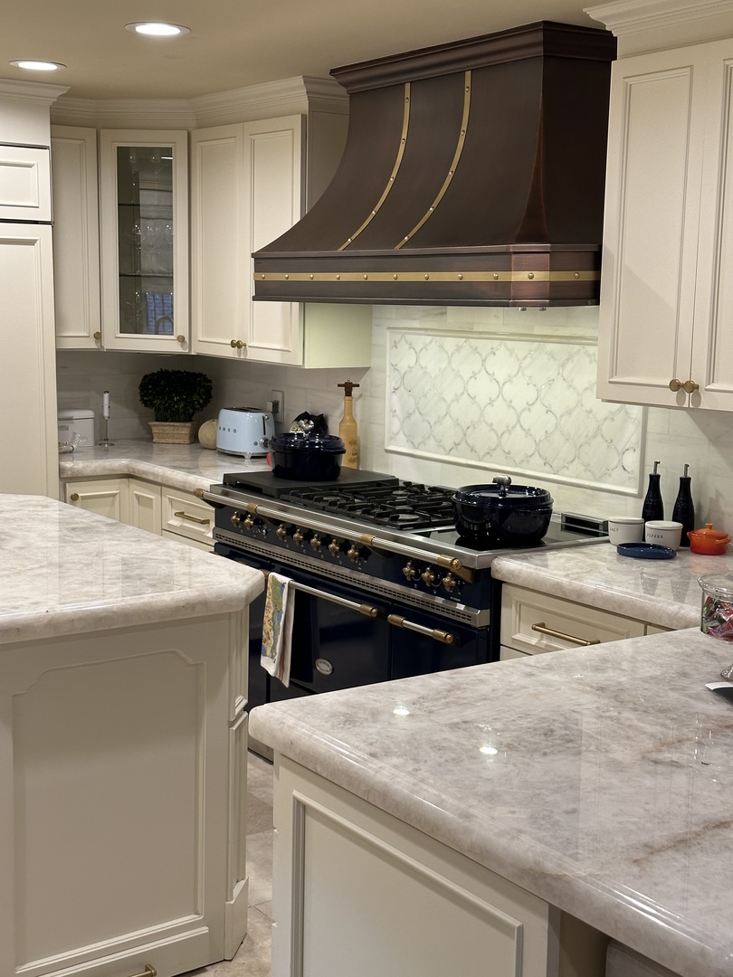 CopperSmith Classic CX4 Antique Copper Range Hood Matte Brass Straps and Rivets in traditional Kitchen with white countertops white tile backsplash and white cabinets