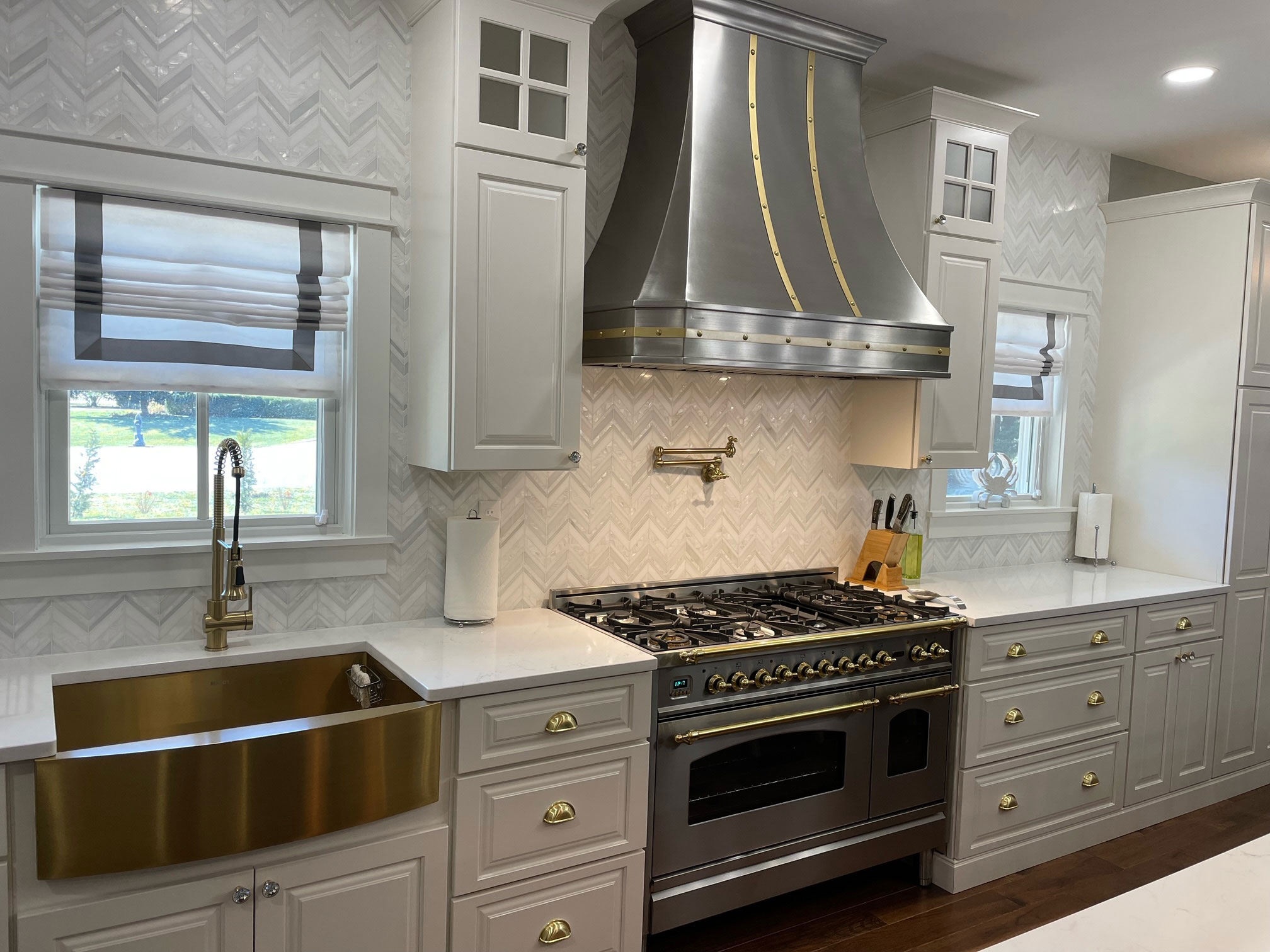 Stainless steel range hood and copper apron sink in a kitchen with white cabinets. World CopperSmit