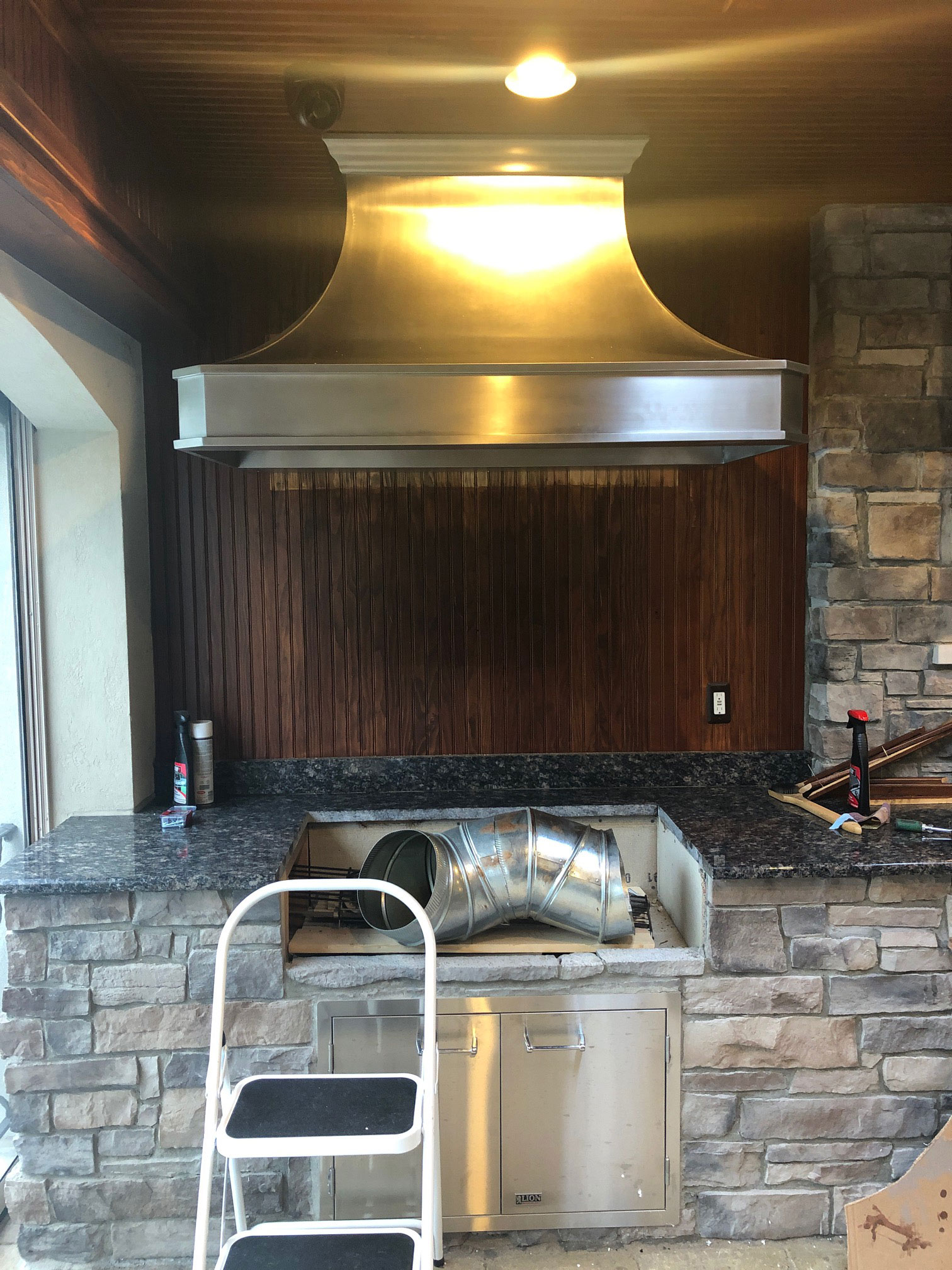 Stainless steel range hood with geometric bell shape in the kitchen with wood paneling