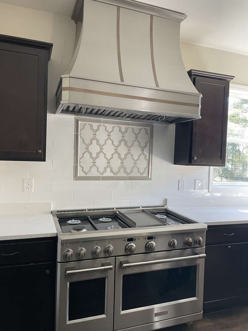 Classic kitchen design with range hood, black cabinets,marble countertops with white tile backsplash