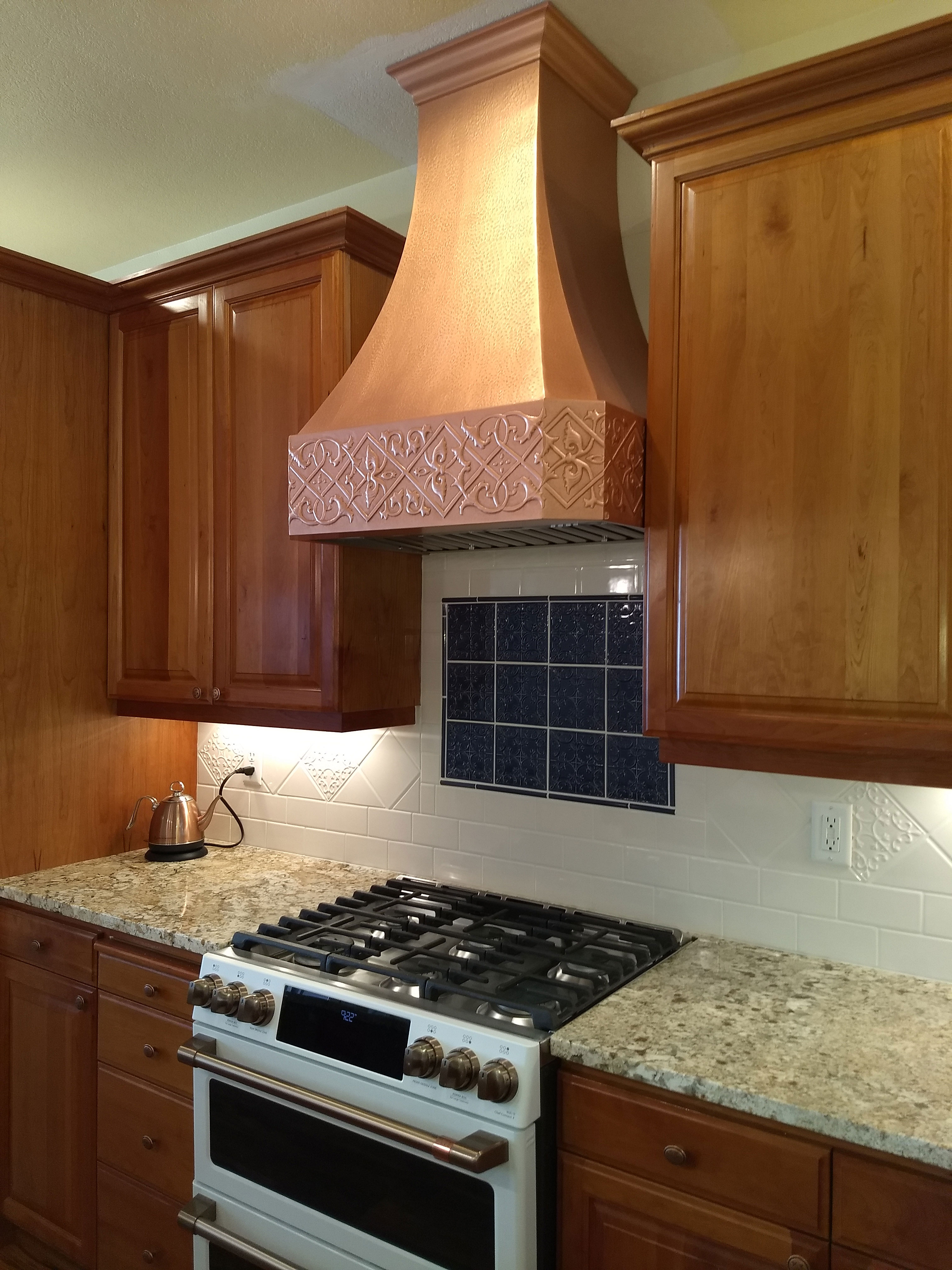 Copper range hood with geometric design in a kitchen with natural wood cabinets. World CopperSmith