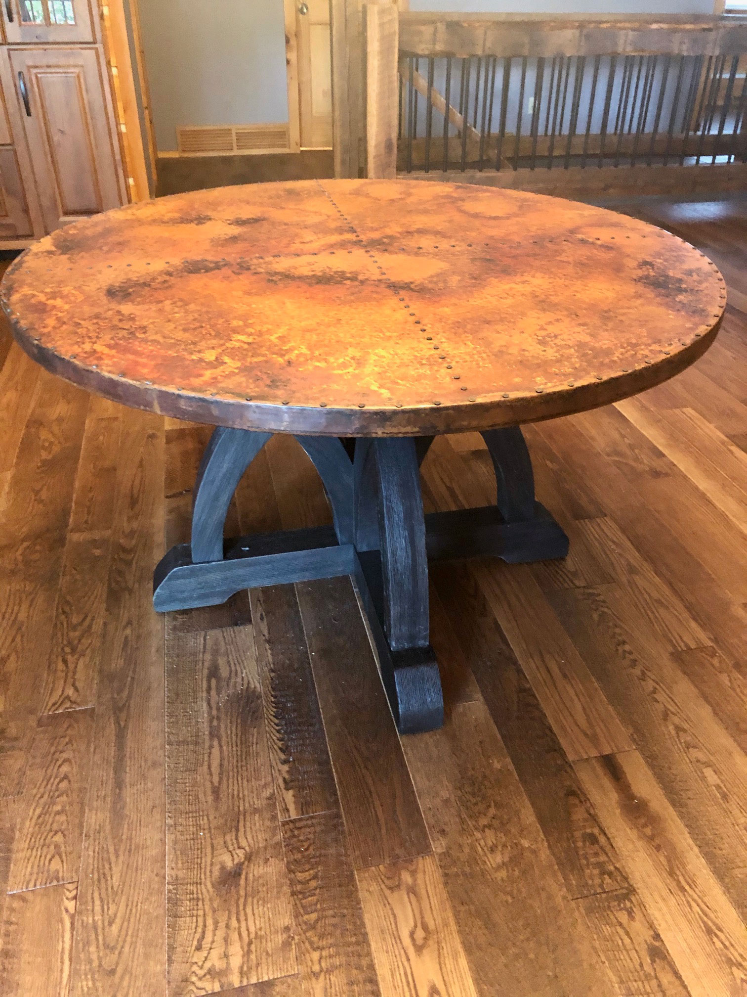 Round copper tabletop with black legs in room with hardwood floors WorldCopperSmith