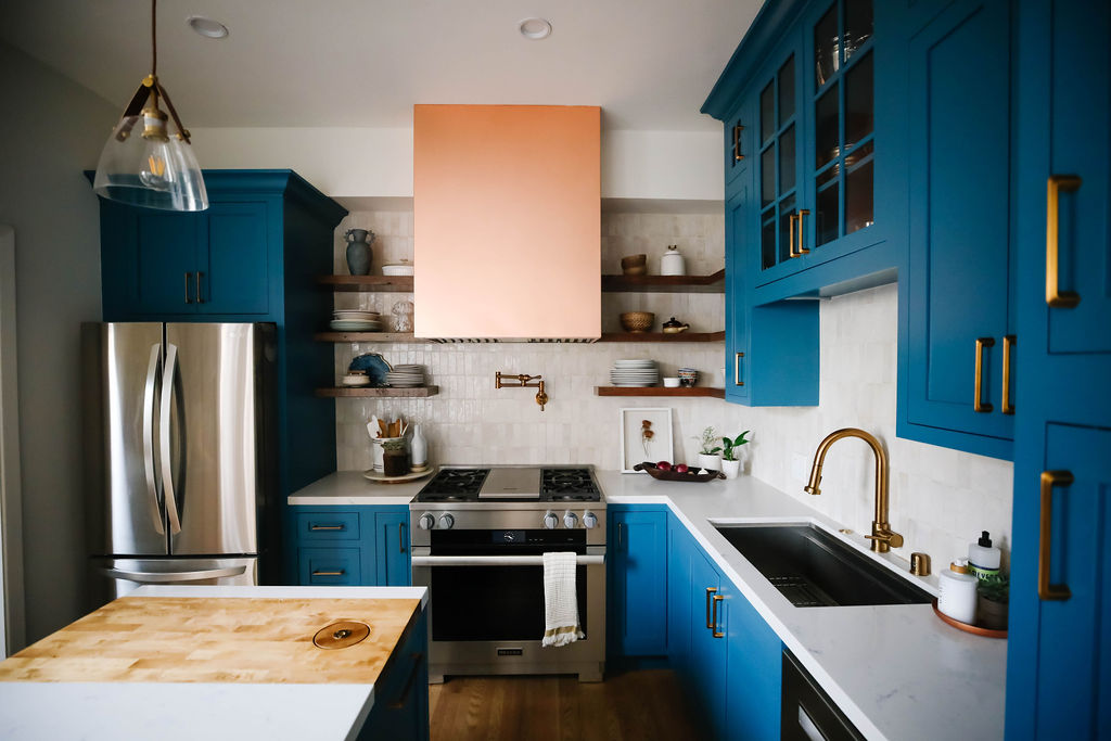 A contemporary kitchen remodel featuring blue kitchen cabinets, marble kitchen countertops, a stylish brick backsplash, and copper range hood