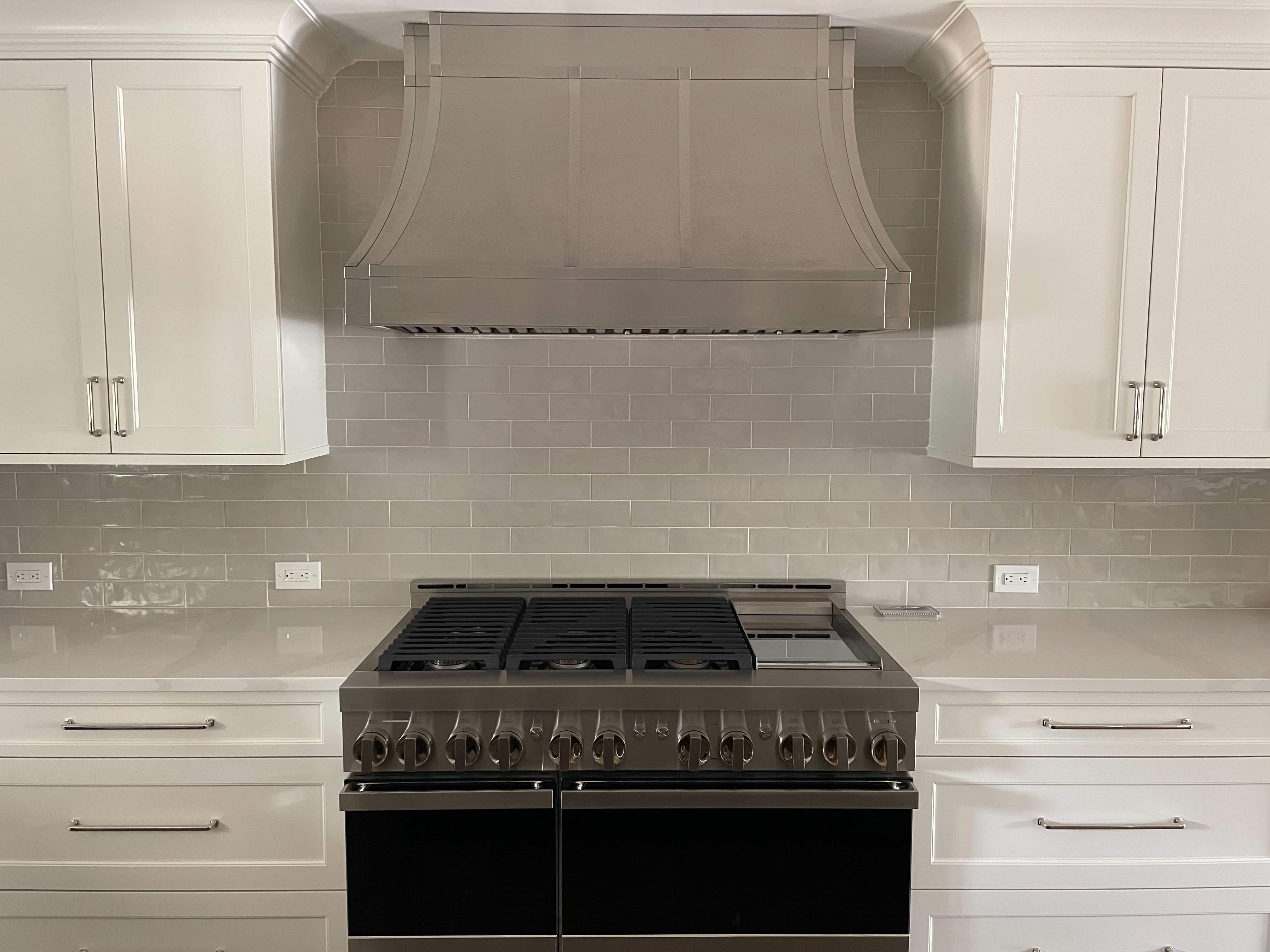 CopperSmith Designer DS6 Brushed Stainless Steel Kitchen Range Hood with Straps in a classic style kitchen features white cabinets tile backsplash white countertops 
