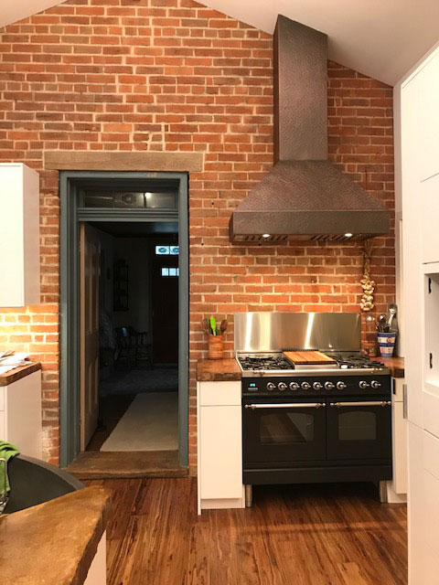 Copper range hood with angular design ign in a kitchen with exposed brick walls  World CopperSmith