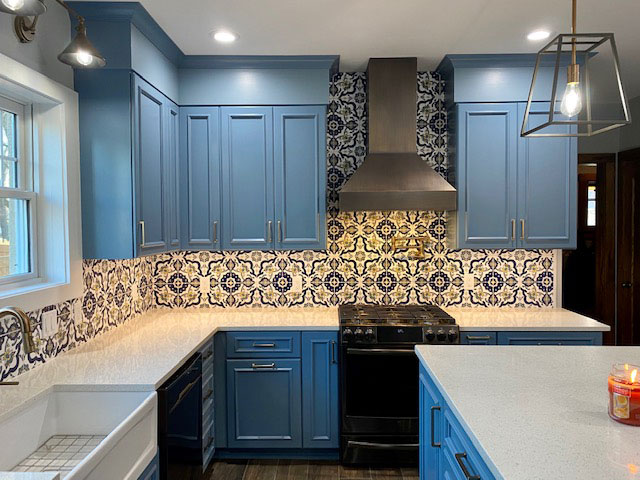Black range hood in a kitchen with blue cabinets and a tile mural. World CopperSmith