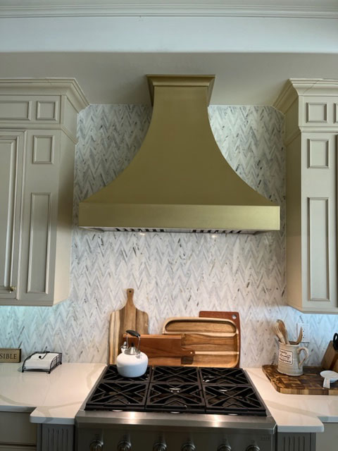 Refined brass range hood in a kitchen with cream cabinets World CopperSmith